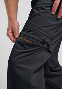 Pantaloni neri da esterno con una tasca laterale con zip visibile. Leggeri, con una superficie liscia e un design strutturato per funzionalità.