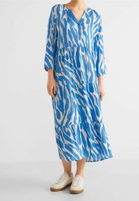 Blå- och vitrandig maxiklänning med V-ringning, trekvarts ärmar och en flerlagers volangkant, i kombination med ljusa sneakers.