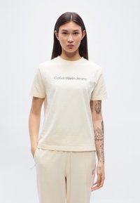 Μπεζ βαμβακερό t-shirt με κοντά μανίκια, με το λογότυπο "Calvin Klein Jeans" σε σκούρο γκρι στο στήθος.