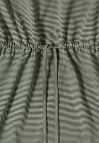 Tissu vert olive avec de fines rayures blanches horizontales et un cordon noué à la taille froncée.