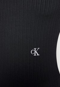 Czarny top z ryflowanej tkaniny z małym, białym, haftowanym logo "cK". Powierzchnia jest gładka z pionowymi liniami.