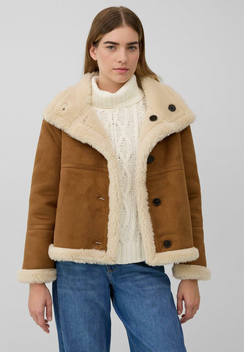 Bruine jas van neppersuède met een pluche, crèmekleurige imitatiebontkraag en boorden, voorzien van zwarte knopen en een cropped ontwerp.