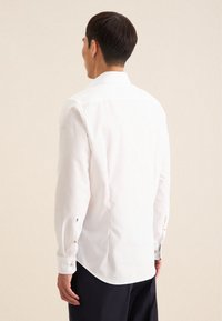 Witte langetermijnshirt met een punthoogte kraag, knopenmanchetten en een licht gebogen zoom; gemaakt van een gladde, lichte stof.