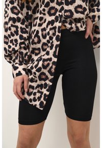 Blusa de leopardo en beige claro con detalles en negro, con un corte relajado y botones, combinada con pantalones cortos de bicicleta ajustados en negro.