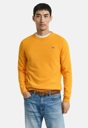 Heldergele gebreide trui met een ronde halslijn, relaxte pasvorm en subtiele geborduurde logo. Gecombineerd met lichtblauwe denim jeans en een leren bruine riem.