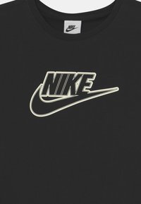 Czarna bawełniana koszulka z dużym białym logo Nike z charakterystycznym znakiem. Okrągły dekolt i krótkie rękawy. Miękka, gładka tekstura.