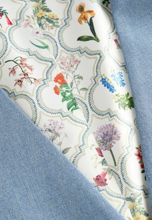 Tissu en denim bleu clair, superposé sur un tissu à motif floral comportant des fleurs de différentes couleurs sur un fond crème avec un bord décoratif.