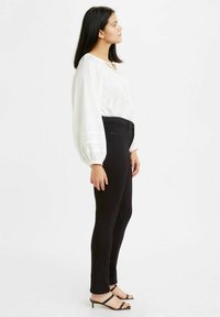 Blusa blanca con mangas abullonadas, combinada con jeans skinny negros y tacones negros de tiras. Diseño sencillo, textura suave y forma ajustada.