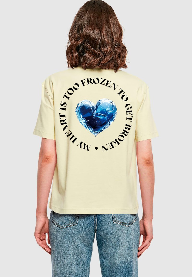 Gul oversized t-skjorte med et blått hjertegrafikk på ryggen, omringet av svart tekst. Stoffet virker mykt, med et avslappet design.