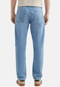 Jean en denim bleu clair à coupe droite, avec deux poches arrière et une texture subtile. Couture distinctive sur les poches.