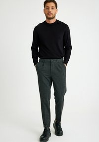 Zwarte trui met lange mouwen, gecombineerd met grijze, gestructureerde broeken met een tapered ontwerp en zijzakken, gedragen met zwarte sneakers.