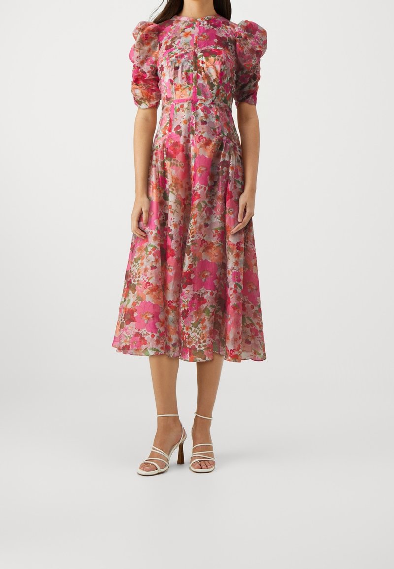 Vestido midi floral con mangas abullonadas, predominantemente rosa con flores multicolores. Tela transparente, corsé ajustado, falda en forma de A, combinado con tacones con tiras.