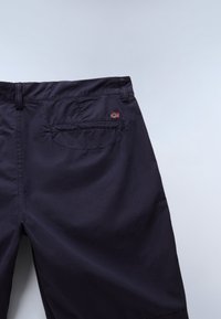 Donkerblauwe broek van lichtgewicht stof met een glad front, zichtbare achterzak en een klein rood-wit logo-accent aan de achterkant.