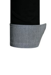 Zwart stoffen overhemd met een grijze, gestructureerde manchetknoop. De manchet is opgerold en toont een lichtgrijs geweven patroon langs de rand.