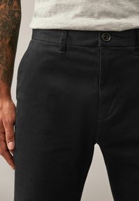 Pantaloni negri cu textură, având o croială clasică, buzunare frontale și o închidere cu nasture la talie. Materialul pare ușor texturat.