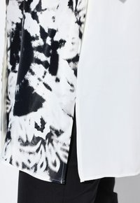 Black and white shirt featuring a watercolor-like print, contrasting textures, and side slits. Made from lightweight fabric.