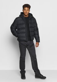 Giacca a vento nera con cappuccio, design trapuntato, zip frontale, indossata sopra un top nero e abbinata a pantaloni scuri e stivali neri.