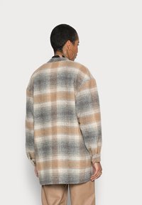 Casaco xadrez oversized em tons de bege, castanho e cinza; tecido texturizado com mangas bufantes e corte reto; vista traseira.