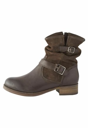 Bottine en cuir et en daim marron avec un col tombant, des boucles sur les côtés et un petit talon en bois. Texture lisse et bout arrondi.