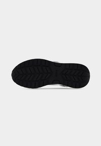 Semelle de chaussure de sport en caoutchouc noir avec un motif texturé et des rainures pour l'adhérence. Présente une marque de logo au centre.