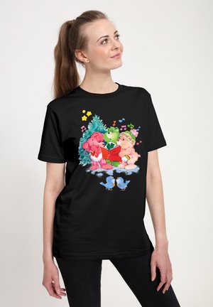 Sort t-shirt med en farverig illustration af tre bjørnefigurer, der synger, med et grønt træ, noder og blåfugle nederst.