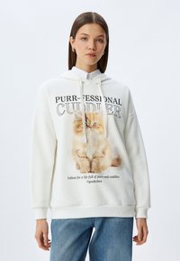 Witte hoodie van zachte stof met een afbeelding van een kat en de tekst "Purr-fessional Cuddler", voorzien van trekkoorden en ribgebreide mouwen.