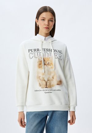 Witte hoodie van zachte stof met een afbeelding van een kat en de tekst "Purr-fessional Cuddler", voorzien van trekkoorden en ribgebreide mouwen.