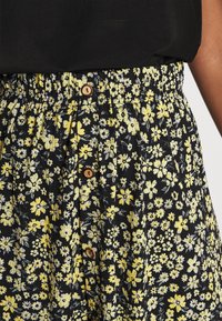 Gonna floreale con sfondo nero caratterizzata da fiori gialli e bianchi. Vita elastica, chiusura con bottone di legno e design plissettato.