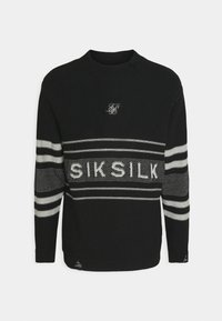 Svart stickad tröja med rund hals, tunna vita ränder och texten 'SIKSILK'. Texturen är ribbad, med små slitna detaljer i nederkant.
