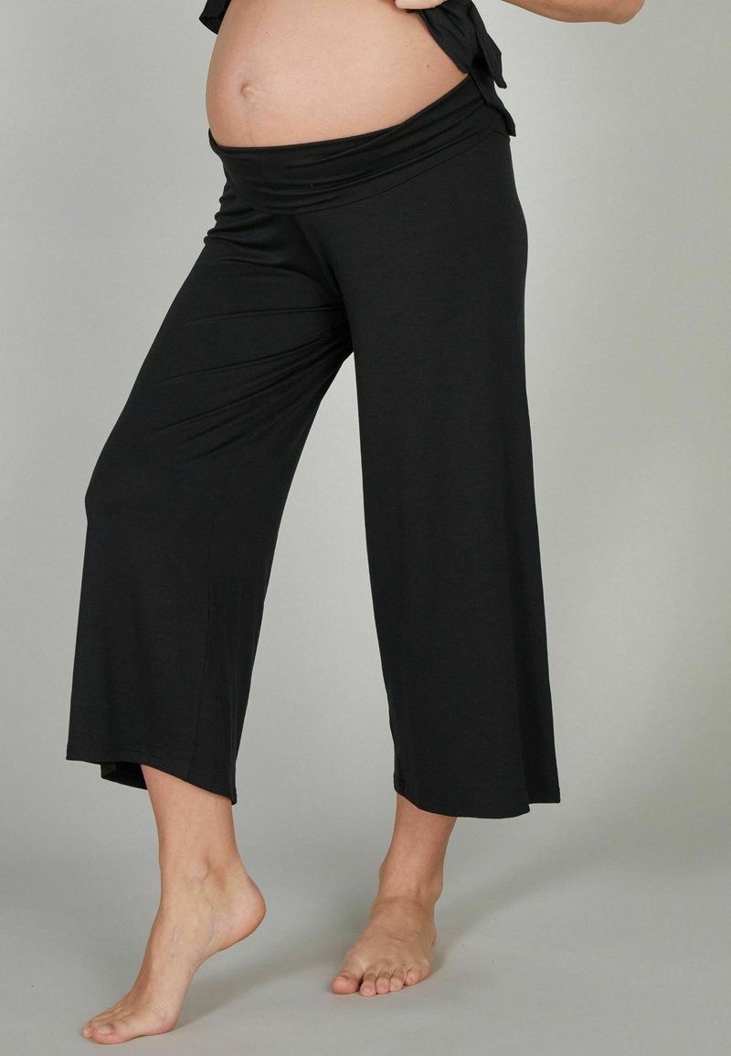 Pantalons de maternité en tissu extensible noir avec une large taille repliable et un design à jambes larges raccourcies. Texture lisse et longueur à la cheville.