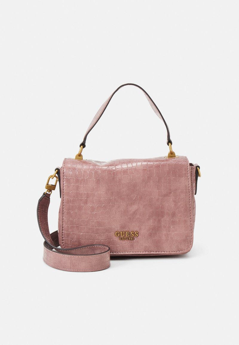Sac à main rose à texture crocodile avec poignée courte et bandoulière longue amovible, garnitures dorées, et logo doré "GUESS EST 1981" sur le rabat avant.