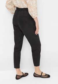 Zwarte tapered broek met een hoge elastische tailleband en twee achterzakken, gecombineerd met zwarte mesh ballerina's. De stof lijkt glad te zijn.