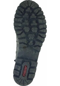 Suela de zapato de goma negra con profundas huellas y un patrón hexagonal; presenta un logo rojo. Superficie texturizada para mayor agarre y durabilidad.
