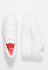 Vita läderplattformssneakers med en texturerad sula, framförande en röd och flerfärgad logodetalj på sidan och vita snören.