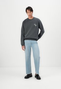 Mørkegrå sweatshirt med rund hals, prydet med et lille grafisk design. Stylet med lyseblå lige ben jeans og sorte sko.