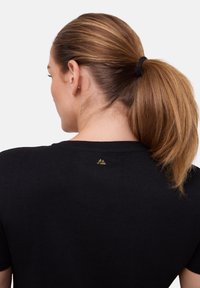 Černé bavlněné tričko s krátkými rukávy, kulatým výstřihem a malým zlatým logem ve tvaru trojúhelníku vzadu poblíž výstřihu.