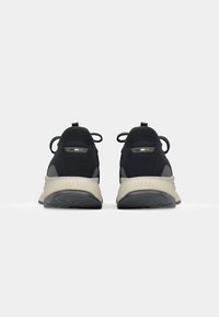 Black athletic shoes with a textured upper, beige midsole, and a patterned rubber sole. Features pull tabs and additional color accents.