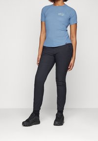 Světlomodré atletické tričko s krátkým rukávem a malým grafikou na hrudi, doplněné tmavými zúženými kalhotami a  černou outdoorovou obuví.