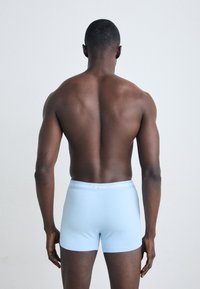 Boxers cortos de color azul claro con una cinturilla blanca de marca, llevados por una persona vista desde atrás. Textura suave y diseño ajustado.