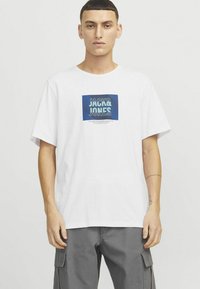 Valge puuvillane t-särk, millel on sinine graafiline kviit "JACK&JONES" tekstiga. Mugav lõige, lühikesed varrukad, sile tekstuur ja ümar kaelus.
