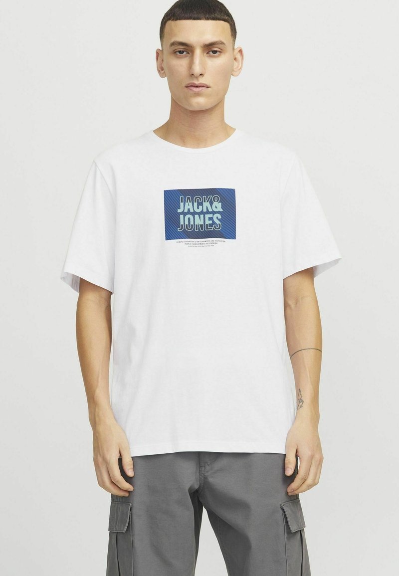 Valge puuvillane t-särk, millel on sinine graafiline kviit "JACK&JONES" tekstiga. Mugav lõige, lühikesed varrukad, sile tekstuur ja ümar kaelus.
