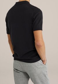 Czarna koszulka polo z krótkim rękawem z teksturowanym wzorem na ramionach, zestawiona z jasnoszarymi teksturowanymi spodniami. Miękka, dzianinowa tkanina.