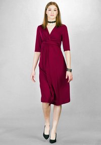 Burgundowa sukienka kopertowa z krótkim rękawem, marszczonym pasem, długością do kolan i gładkiego materiału. Noszona z czarnymi szpilkami i naszyjnikiem chokers.
