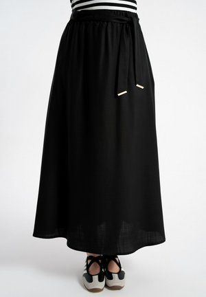 Czarna spódnica midi z wiązanym paskiem w talii, noszona z paskowanym topem i czarno-białymi balerinami, stojąca na białym tle.