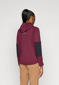 Hoodie cor de vinho com detalhes em preto nas mangas, apresentando um capuz com cordão e um logotipo nas costas. Feito de um tecido texturizado, adequado para uso ao ar livre.