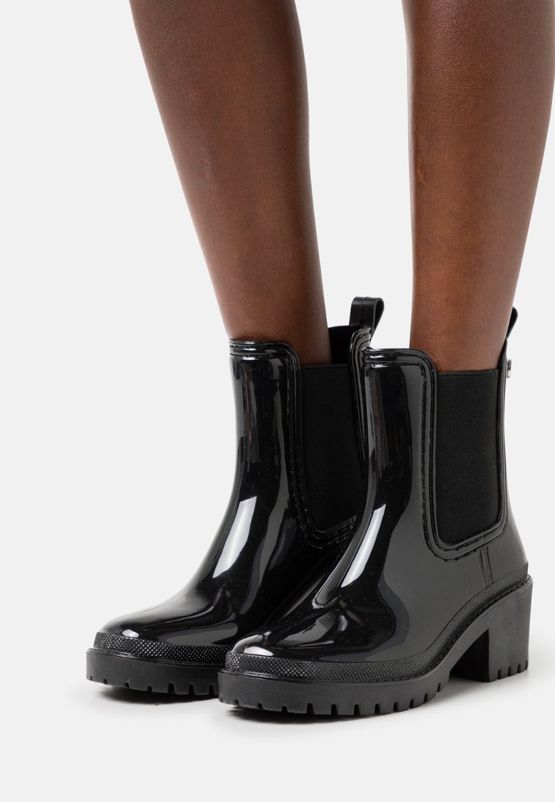 Black patent leather ankle boots with elastic side panels, chunky heels, and textured soles; smooth finish with pull tab detail.