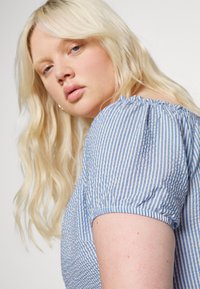 Blusa às riscas azul e branca com mangas bufantes e decote franzido. Tecido suave e texturizado com um corte casual.
