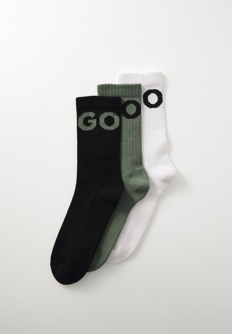 Trois paires de chaussettes : noires avec le texte "GO" en vert, vert olive avec un "O" vert foncé, et blanches avec un "O" noir. Texture côtelée, hauteur mi-mollet.