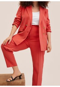 Coral blazer and matching tapered pants in smooth fabric, featuring a double-breasted design and gold buttons, paired with black heeled sandals.