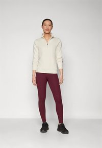 Lichtbeige half-ritssweatshirt en bordeauxrode leggings, met een aangesloten ontwerp en een zachte textuur, gecombineerd met zwarte sportschoenen.